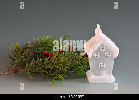 Weihnachtsdekoration in Form eines weißen, schneebedeckten Hauses und Weihnachtszweigs vor buntem Hintergrund Stockfoto