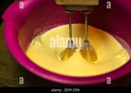 Elektrischer Handmixer, der gelben Teig in rosafarbener Rührschüssel schlägt Stockfoto