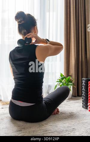 Junge Frau, die zu Hause auf dem Boden sitzt und einen Massageball benutzt, um Nackenschmerzen zu lindern. Selbstpflegeroutine für Muskelverspannungen und Halswirbelsäulengesundheit. Stockfoto