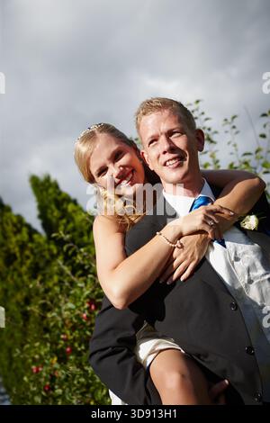 Lächeln, Paare und Huckepack bei der Hochzeit im Freien für Liebe, Feier und Heiratsverpflichtung. Porträt, Menschen und verspielte Tradition für Romantik Stockfoto