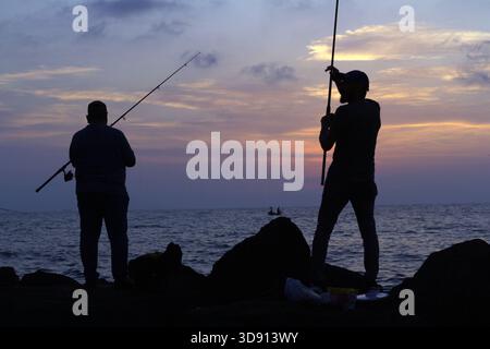 Fischer Silhouetten Casting Lines at Sunset zwei Männer in Silhouette fischen bei Sonnenuntergang von einer felsigen Küste aus Stockfoto