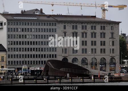 Eine Reihe von Bürogebäuden mit vielen Fenstern steht am Hafen in Helsinki, Finnland, mit Baukränen und bedecktem grauem Himmel im Hintergrund. Stockfoto