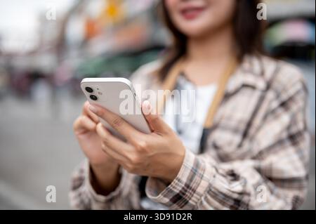 Nahaufnahme einer Touristenfrau in einem Scotch-Hemd, die ihr Handy überprüft, während sie auf einem lokalen Markt an der Straße steht. Fußgängerstraße, Ausflug in die Altstadt. Stockfoto
