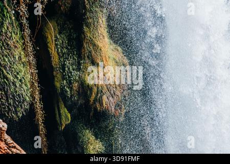 Abstrakte Nahaufnahme von Wasserspray und Nebel gegen leuchtendes Grün und Orange moosbedecktes Gestein, horizontales Detail Stockfoto