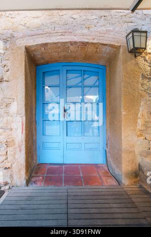 Leuchtend blaue Doppeltür in rustikalem Bogenstein und Stuckeingang mit Terrakotta-Fliesen und Holzboden, Außenlaterne Stockfoto