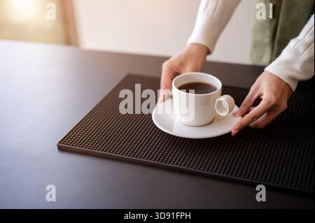 Nahaufnahme eines Barista oder Kellners, der eine Tasse Kaffee auf den Tisch legt und einem Gast an der Theke serviert. Café oder Café-Bar, kleine Unternehmen. Stockfoto