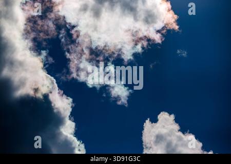 Eine kraftvolle Komposition mit hellen, weißen und grauen Cumulus-Wolkenstrukturen, die in einen riesigen, tiefblauen Sommerhimmel mit Anklängen von subtiler Iris platzen Stockfoto