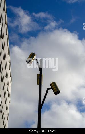 Moderner Schwarzlichtpfosten mit drei verschiedenen goldenen, zylindrischen Lampen vor einem blauen Himmel mit dramatischen weißen Wolken. Stockholm, Schweden. Stockfoto