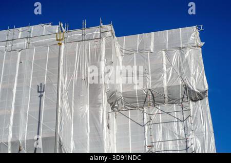 Ein großes Gebäude in Stockholm, Schweden, das umfassend renoviert wird, komplett mit weißen Kunststofffolien umhüllt und von Gerüstbau ag gestützt wird Stockfoto