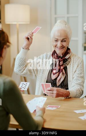 Ältere Frau lächelt, während sie Karten mit jungen Erwachsenen spielt Stockfoto