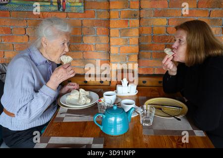 Porträt einer 90-jährigen grauhaarigen Seniorin, die in einem Restaurant mit Tochter speist. Suppe, Hauptgericht, Tee. Unterhaltung. Stockfoto