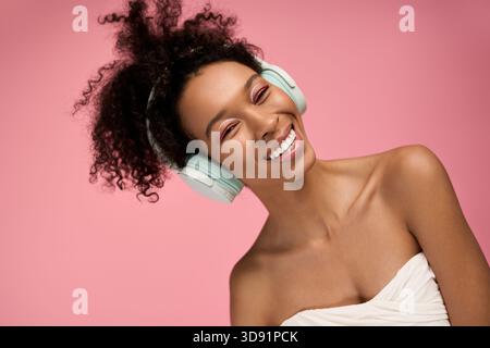 Mit einem strahlenden Lächeln taucht eine junge Frau mit pastellfarbenen Kopfhörern in fröhliche Musik ein. Stockfoto