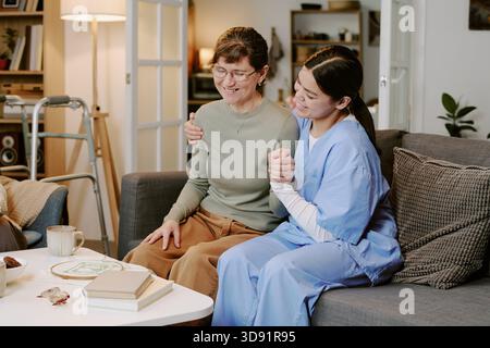 Frau mittleren Alters umarmt Seniorin auf Sofa lächelnd Stockfoto