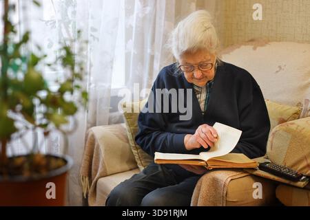 Eine ältere Frau, die zu Hause in einem bequemen Sessel ein Buch liest Stockfoto