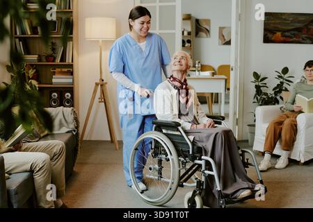 Ältere Frau mit Behinderung lächelt, während die Schwester drinnen hilft Stockfoto