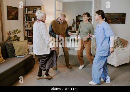 Gruppe von Senioren und jungen hispanischen Frauen, die zusammen im Wohnzimmer tanzen Stockfoto
