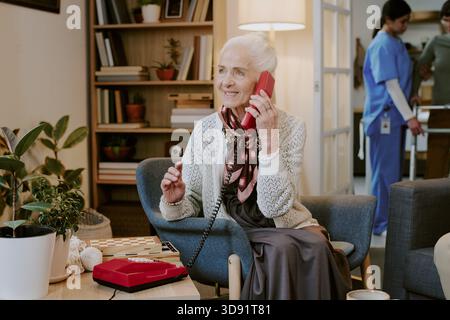Eine ältere Frau lächelt, während sie im Festnetz telefoniert Stockfoto