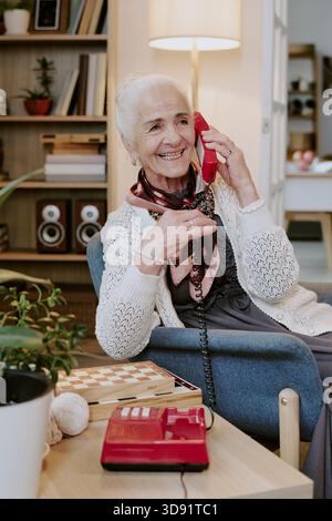 Seniorin lacht, während sie drinnen über schnurgebundene Telefone plaudert Stockfoto