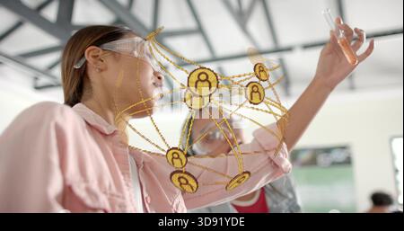 Orangene Flüssigkeit im Reagenzglas untersuchen, Frau mit rosa Hemd, Brille im Labor mit goldenem Überzug Stockfoto