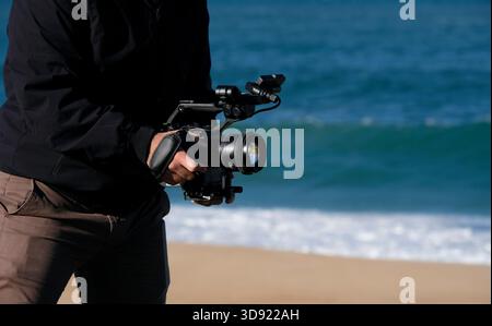 Kameramann filmt am Strand an einem sonnigen Tag mit einer DSLR-Kamera Stockfoto