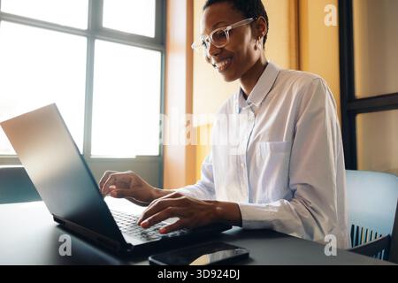 Eine junge professionelle Frau mit Brille arbeitet mit Begeisterung an einem Laptop in einem Büro. Stockfoto