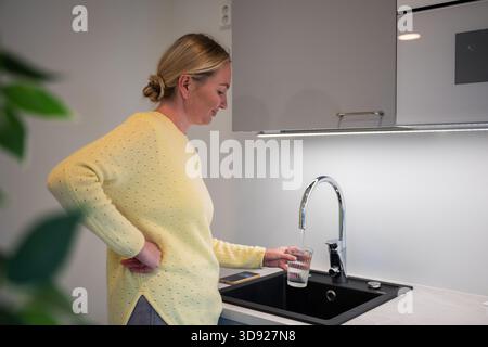 Frau, die Glas mit Wasser aus dem Küchenhahn füllt Stockfoto