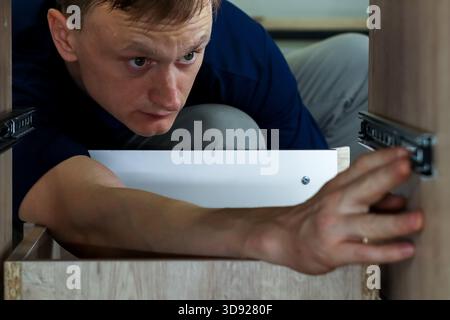 Furniture assembler adjusting drawer slide mechanism. Carpenter fine-tuning metal drawer runner while installing wooden drawer in cabinet. Stockfoto