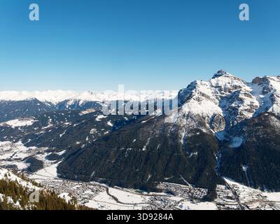 Schneebedeckte Bergkette unter klarem blauen Himmel mit schneebedeckten Gipfeln und Valley Town Stockfoto