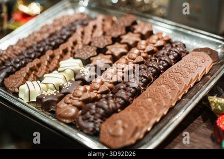 Weihnachtsmotive und geformte Schokoladensortiment auf einem silbernen Tablett im Schaufenster. Nahaufnahme, geringe Tiefe, wenn Feld, keine Personen Stockfoto