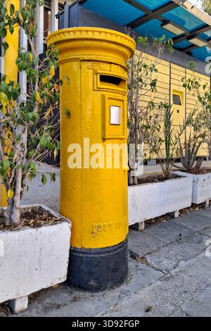 Gelb zypriotischer Säulenkasten neben einem Paketschließfach vor einem Postamt. Stockfoto