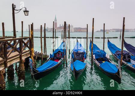 Nebeliger Winterblick auf den Canal Grande in Venedig, Italien. Geparkte traditionelle lange Holzboote Gondeln. Türkisfarbenes Wasser und Stadtbild von Venedig. Stockfoto