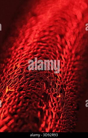 Künstlerische Makroaufnahme von Wassertröpfchen unter rotem Licht, die eine leuchtende abstrakte Textur bilden. Stockfoto