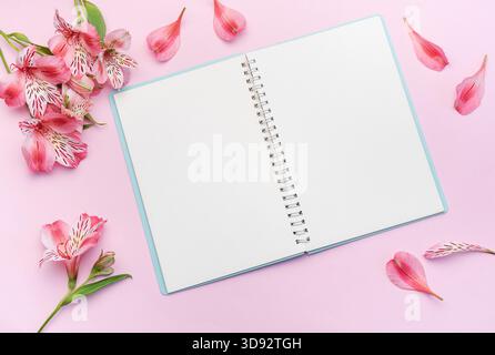 Das Notizbuch, umgeben von rosa Alstroemeria-Blumen und -Blüten auf rosa Hintergrund Stockfoto