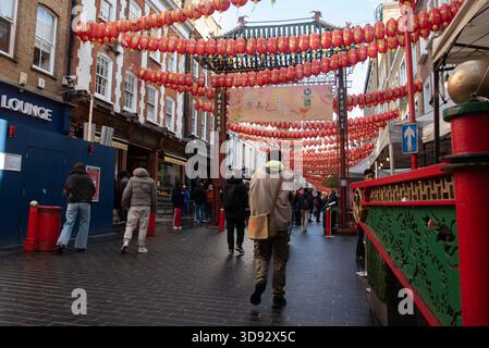 London, Vereinigtes Königreich, 23. November 2025: Menschen, die unter dem traditionellen chinesischen Bogen spazieren, umgeben von Läden und Laternen Stockfoto