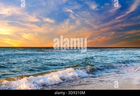 Wunderschöner Sonnenuntergang über Meer oder Meer. Lebendige und weiche Farben, magisches Licht. Kleine Wolken am Himmel, Spiegelung der Sonne im Wasser und Sand am Strand. Stockfoto