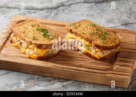 Hausgemachte Thunfischschschmelze-Toasts aus Butterbrot, Thunfischkonserven mit Gemüse, Mayonnaise und geschmolzenem Käse in Nahaufnahme auf einem Holzbrett auf dem Tisch. Stockfoto