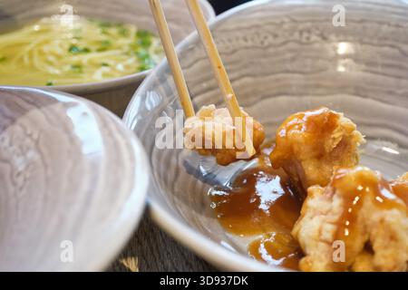 Essstäbchen zum Aufnehmen von knusprigem, gebratenem Hähnchen in süßer Sauce aus der Schüssel Stockfoto