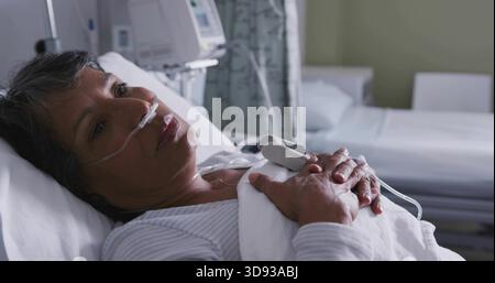 Ruhende Seniorin liegend im Krankenhausbett, in gestreifter Oberseite mit Nasenkanüle und Pulsoximeter Stockfoto