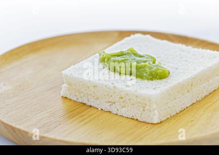 Eine Nahaufnahme einer dicken Scheibe Weißbrot mit einem Pandan-Pudding auf einer runden Holzplatte vor einem sauberen weißen Hintergrund. Stockfoto