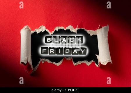Eine Nahaufnahme des „Black Friday“-Schildes mit einem im Dunkeln leuchtenden Effekt auf gerissenem rotem Papier. Hochauflösendes Foto. Stockfoto