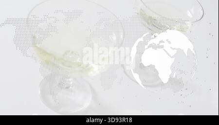 Zeigt drei Stielgläser mit blassgelber Flüssigkeit und Eis auf weißem Tisch, Überlagerung der Globus-Karte Stockfoto