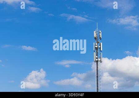 Hoher Telekommunikationsmast mit 5G- und 4G-Antennen vor einem hellblauen Himmel mit weißen Wolken, der die globale digitale Konnektivität symbolisiert. Stockfoto
