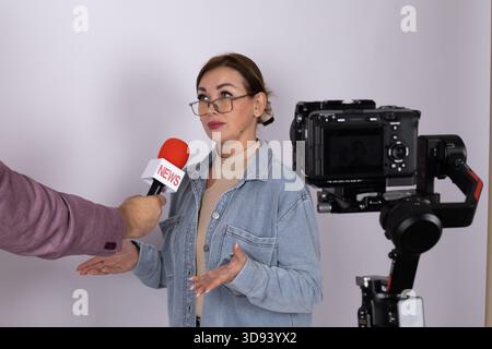 Eine Reporterin hält ein Mikrofon, bereit, ein Interview mit einer Videokamera zu führen Stockfoto