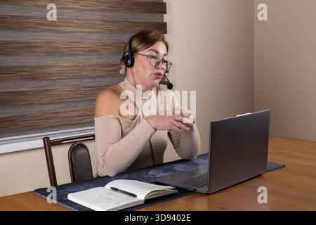Geschäftsfrau in einem Headset, die in einem hellen Heimbüro an einem Laptop arbeitet Stockfoto
