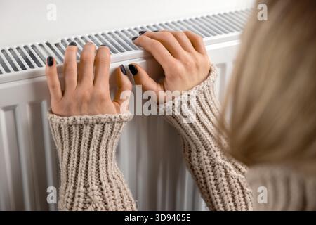 Frau wärmt die Hände auf dem Heizkörper zu Hause. Heizsaison Stockfoto