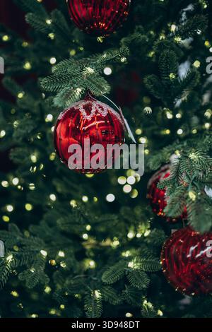 Nahaufnahme eines Weihnachtsbaums mit leuchtenden Lichtern und glänzenden roten Ornamenten, die eine festliche und warme Feiertagsatmosphäre schaffen. Stockfoto
