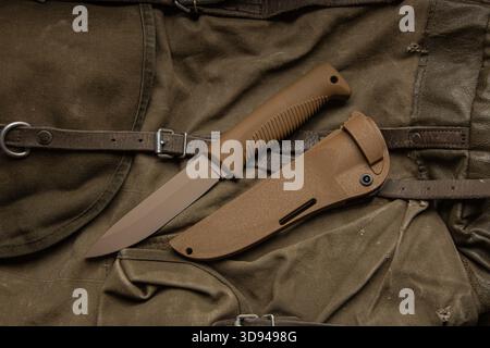 Braunes taktisches Messer mit fester Klinge oder Überlebensmesser mit seiner Ummantelung auf einem Leinentasche. Stockfoto