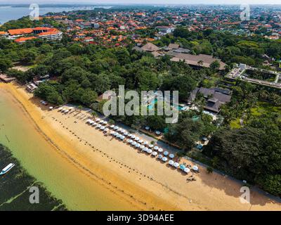 Blick auf einen goldenen Sandstrand und ein üppiges, grünes tropisches Resort in Sanur, Bali Stockfoto