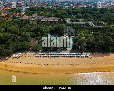 Blick auf Sonnenschirme an einem goldenen Sandstrand neben einem üppigen Resort auf Bali Stockfoto