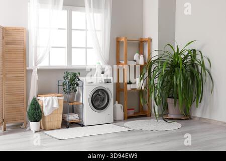 Waschmaschine, Wäschekorb und Klappschirm neben dem Fenster im Zimmer Stockfoto